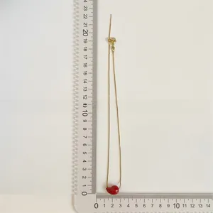 Detailed view of a gold chain necklace with a red teardrop pendant measured with a ruler