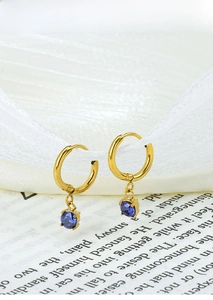 Close-up of gold hoop earrings with blue round gemstones on a decorative background