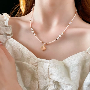 Detail of beaded necklace with 18K gold-plated sun pendant and pink-white beads