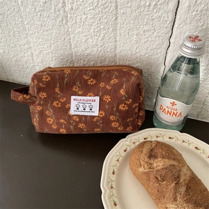 Détail d'une trousse à maquillage en velours côtelé fleuri avec poignée latérale