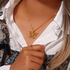 Close-up of golden butterfly pendant necklace and sparkling black gemstone ring on model