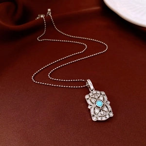 Detail of silver hollow pendant with blue center stone and intricate flower engravings