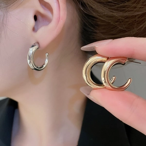 Macro detail of C-shaped metallic hoop earrings in silver, gold and rose gold