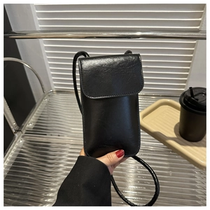 Close-up of a minimalist black leather crossbody phone bag with flap and thin shoulder strap