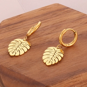 Detaillierte Ansicht goldener Monstera-Blatt-Ohrringe auf einem dunklen Holzständer
