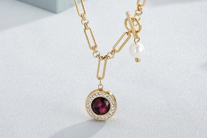 Detail of gold chain necklace with toggle clasp, red gemstone and white pearl pendant