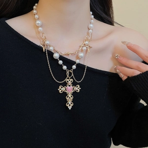 Close-up of layered pearl necklace featuring a gold cross pendant with pink heart gemstone