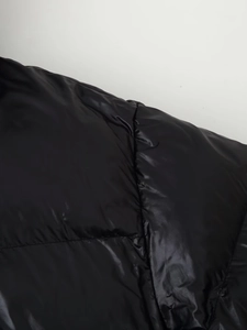 Detailed close-up of black glossy fabric and horizontal stitching on hooded puffer coat