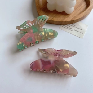 Pink and green acetate butterfly hair claw clip displayed on a wooden tray decor