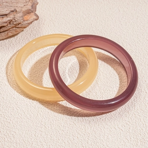 Detail of amber yellow and purple resin geometric round bangles on a textured surface