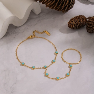 Gold stainless steel finger chain bracelet with turquoise beads on marble surface