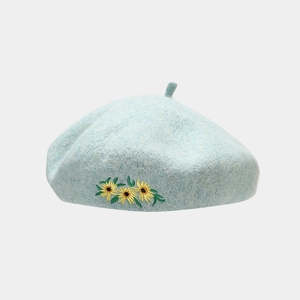 Detail von drei gelben Sonnenblumen-Stickereien auf einer hellblauen Baskenmütze