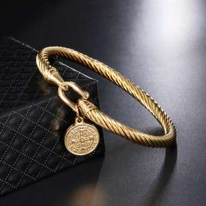 Golden twisted cable bracelet with St. Benedict religious pendant on a black jewelry box