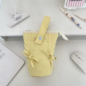 Macro shot of pale yellow fabric pencil case with decorative bow and handle on workspace