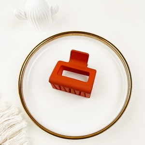 Top view of matte orange rectangular hair claw clip on a decorative gold-rimmed white plate