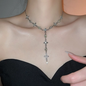 Detailed close-up of a silver cross Y-necklace with green crystals and a teardrop pendant