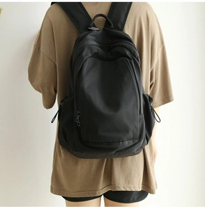 Rear view of a model wearing a large black minimalist nylon backpack on a white background