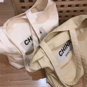 Sacs cabas en toile kaki et beige avec imprimé China posés sur un sol en bois