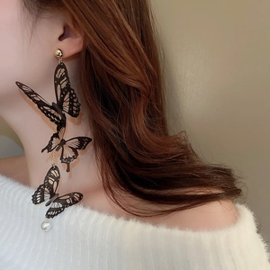 Vue rapprochée de boucles d'oreilles à pompons, papillons noirs et perle sur mannequin