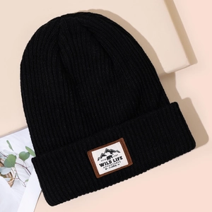 Winter warm knitted beanie with jacquard stripes and wild adventure patch on beige background