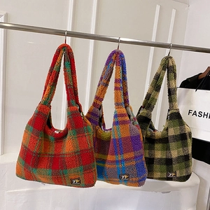 Three oversized plaid plush tote bags in autumn colors hanging on a minimal display