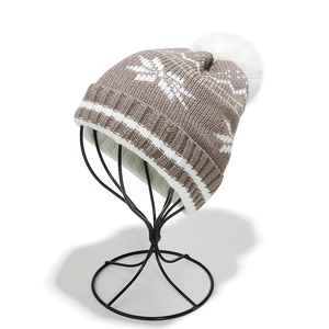 Close-up of knit winter hat texture with white snowflake patterns and a soft pom-pom