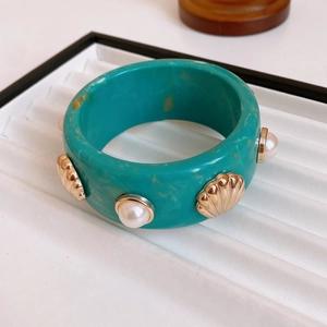 Close-up of turquoise resin bangle with inlaid gold shell and pearl decorations