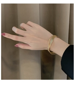Dettaglio di un bracciale aperto in oro opaco con design a doppia fibbia incrociata al polso