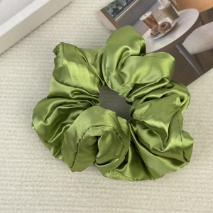 Detailed close-up of a green satin silk hair scrunchie with soft fabric pleats and glow