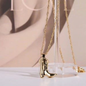 Detailed close-up of golden cowboy boot pendant with water wave chain on a display stand