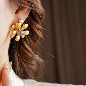 Close-up of gold flower petal earrings with a purple pearl center on a model