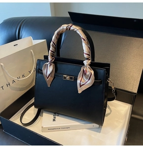 Detail of a black leather tote with a silk scarf handle and gold hardware in a gift box