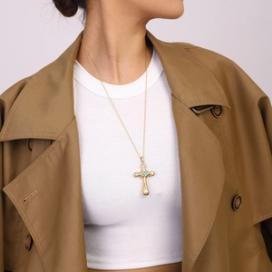 Macro detail of gold cross pendant featuring blue and clear zircon stones on a model