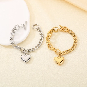 Detail of gold and silver chunky chain bracelets with heart charms and OT clasp