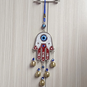 Detail of red Hamsa hand wall hanging with blue evil eyes and small brass bells decoration