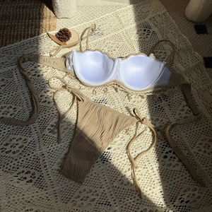 Detail of beige pleated bikini top featuring scalloped edges and tiny decorative seashells