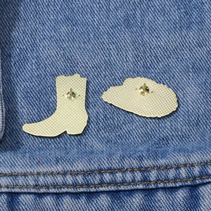 Golden enamel cowboy boot and hat pins shown with back needle detail on denim fabric