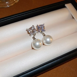 Detail shot of square-cut zircon and white pearl drop earrings in a black jewelry box