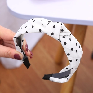 Dettaglio del cerchietto in tessuto bianco a pois neri con nodo tenuto da una mano