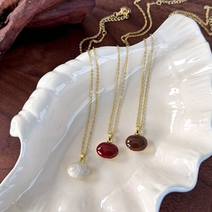 Three minimalist bean necklaces in red, white, and brown on a white shell tray