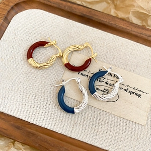 Detail of twisted metal hoop earrings with burgundy and navy blue enamel finish