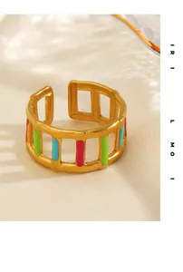 Dettaglio macro di anello dorato traforato con smalto rosa, verde e blu su seta