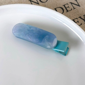 Close-up of blue marble resin hair clip with gold glitter details and metal base