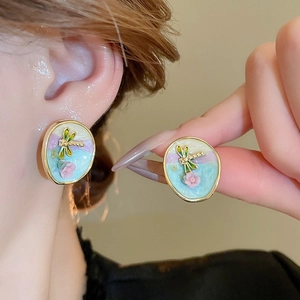 Detailed shot of enamel flower earrings with gold dragonfly accents on a model's ear