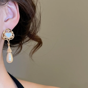 Close-up of elegant gold heart and teardrop pearl earring worn on a model's ear