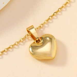 Polished gold heart pendant necklace on soft pink background, minimalist jewelry accessory