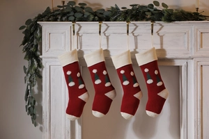 Detail of four red and white knitted Christmas stockings with 3D hat hanging on mantel