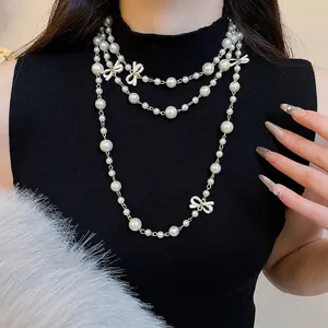 French style layered pearl necklace with white enamel bows and golden chain on black sweater