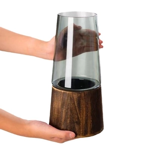 Clear gray glass vase with dark wood base held by hands on a clean white background