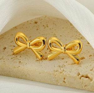 Macro shot of 18K gold bow-shaped stud earrings on a beige stone surface